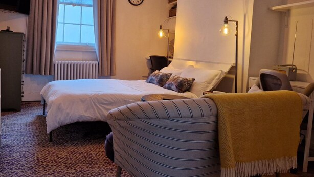 A hotel room with two beds, a striped armchair, a yellow throw, a clock, and a radiator. - Charming Studio Sleeps 2 - Kentish Town Nwlondon (London)