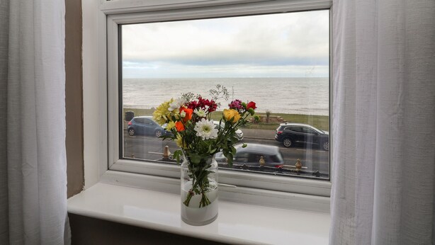 A window with a vase of flowers and a view of the sea.
