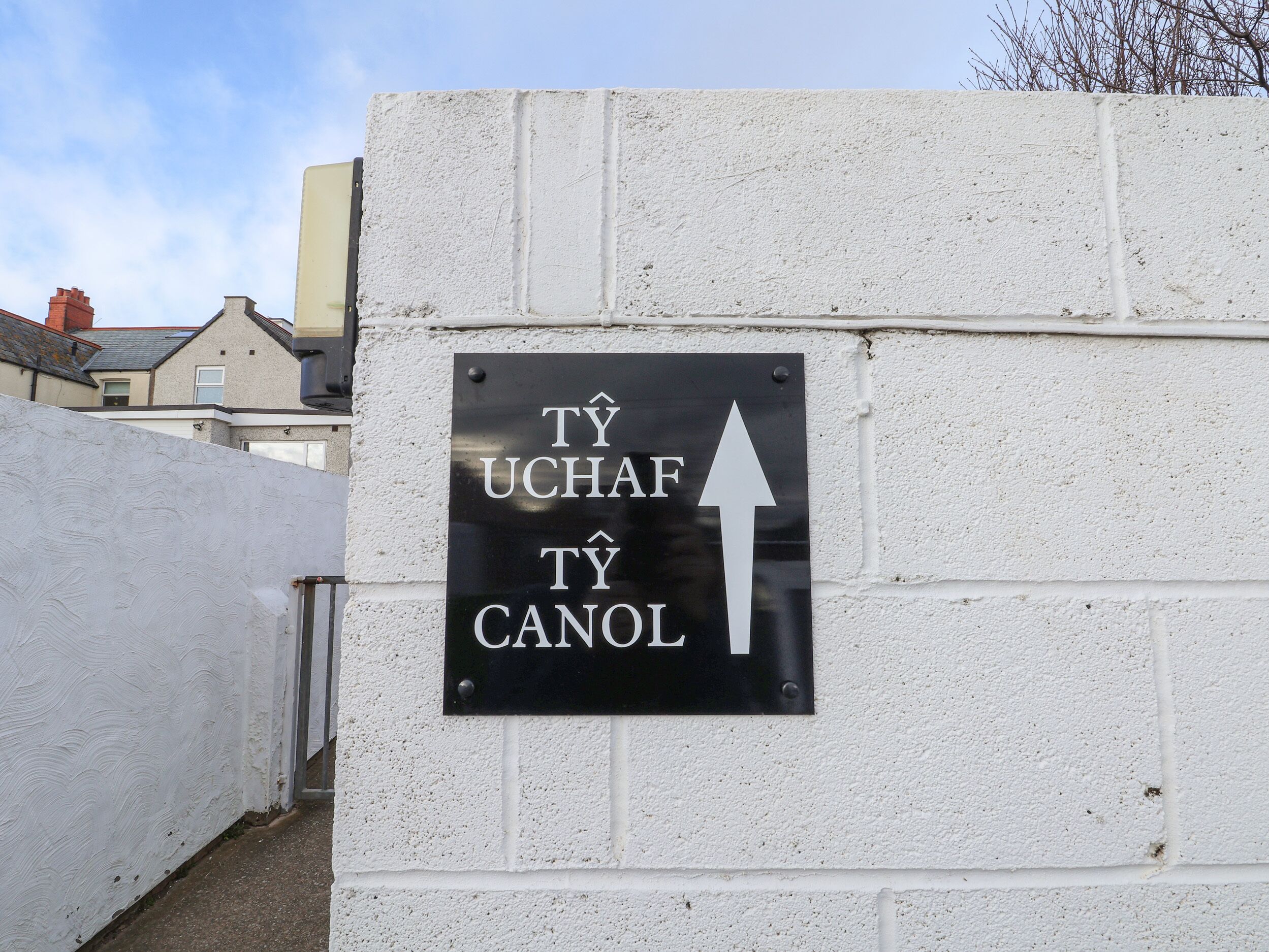 A directional sign on a white wall with an arrow pointing upwards, indicating the direction to the entrance.