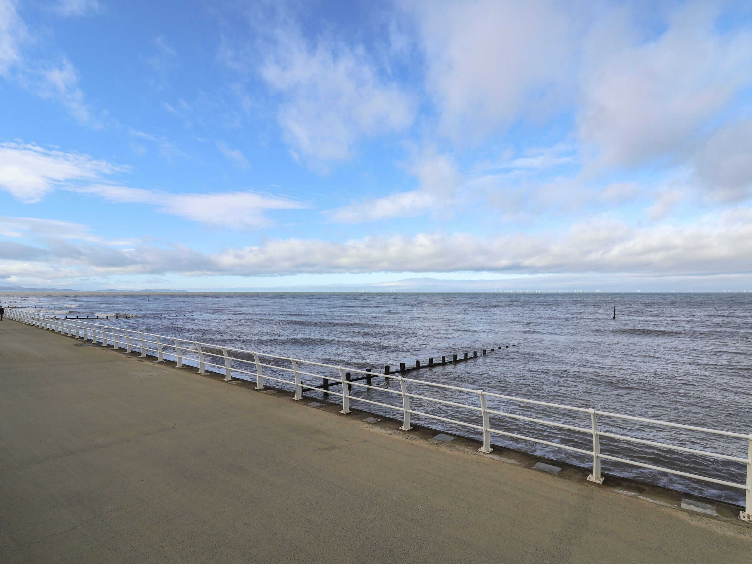 A coastal walkway with a metal railing, leading to the sea.