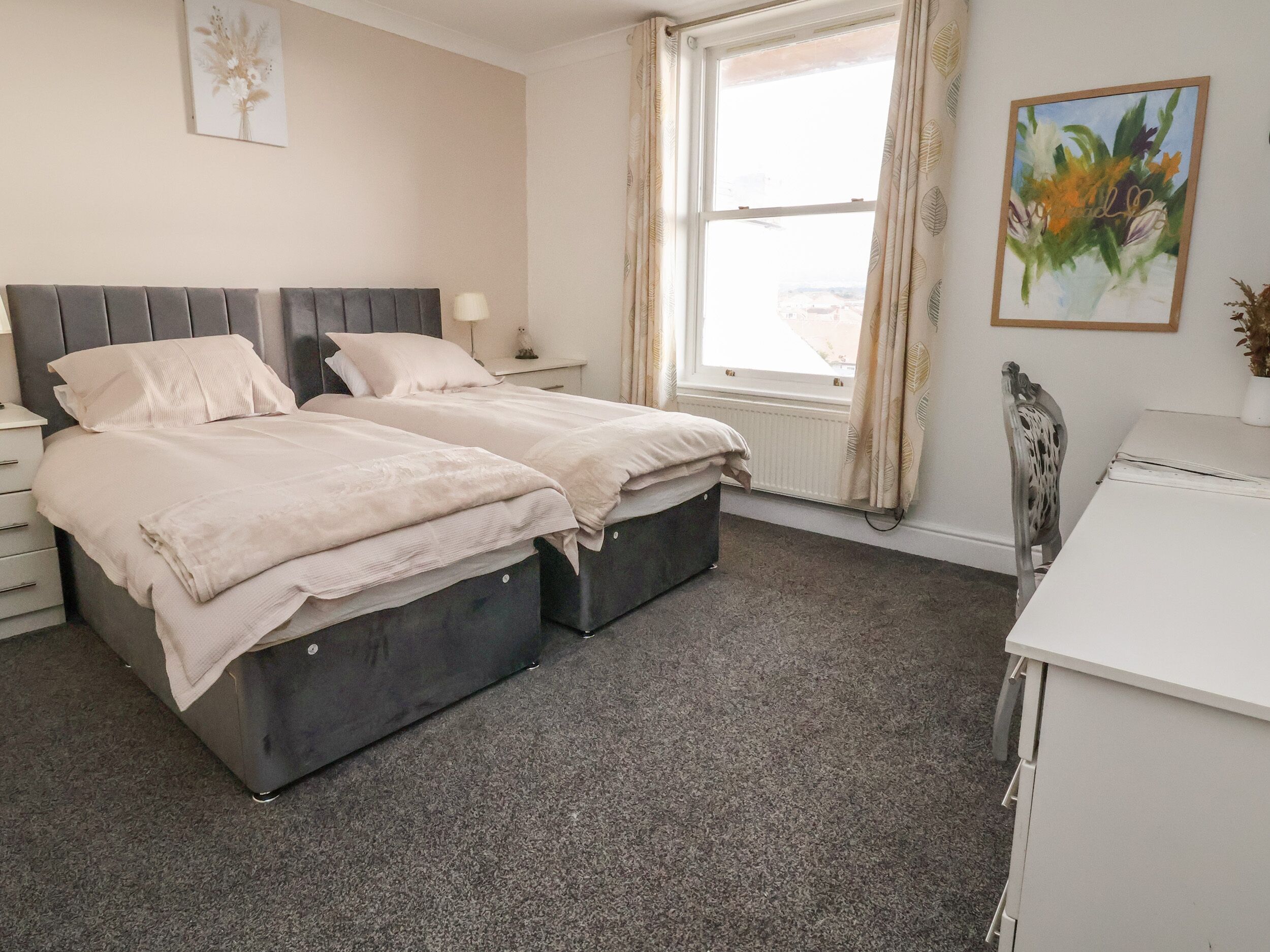 A bedroom with two beds, a desk, and a window with curtains.