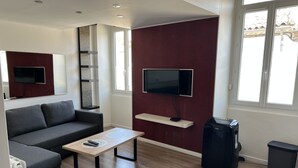 Un salon moderne avec un canapé gris, une table basse en bois, un téléviseur fixé sur un mur rouge et un haut-parleur noir.