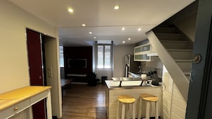 Une cuisine compacte avec un plancher en bois, un téléviseur encastré et un petit coin bar avec des tabourets.