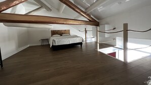 Une chambre spacieuse située sous les combles, avec un grand lit, des poutres apparentes et une vue sur le ciel.