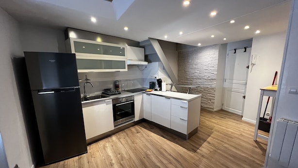 Une cuisine moderne avec un réfrigérateur noir, des appareils électroménagers en acier inoxydable et un plancher en bois.