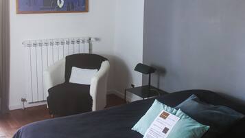 Une chambre à coucher avec un lit, une chaise, un radiateur, un ventilateur de plafond et un tableau accroché au mur.
