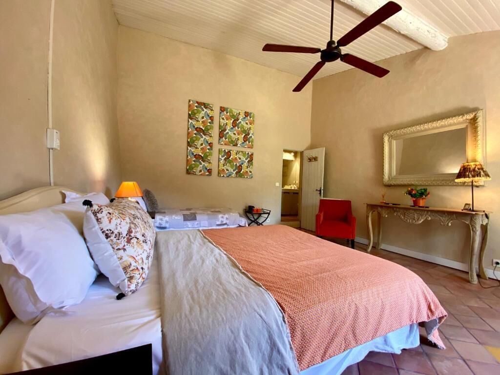 A bedroom with a bed, a ceiling fan, a mirror, and artwork on the wall.