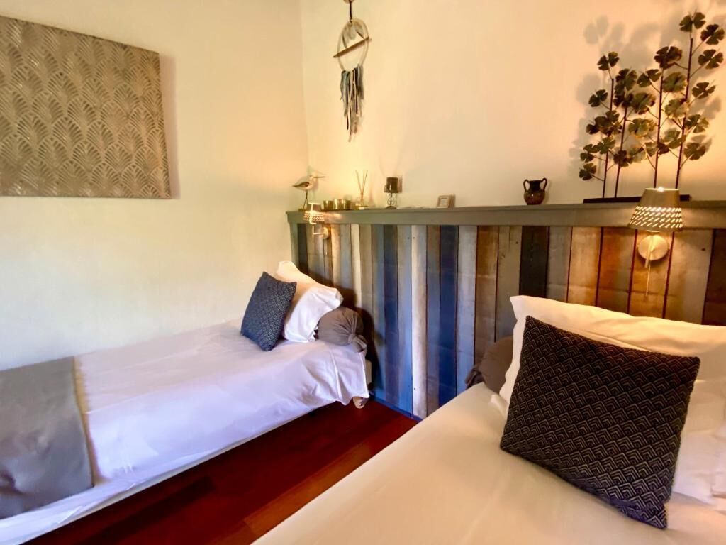 A room with two beds, a wooden headboard, a wall-mounted dreamcatcher, and a decorative plant.