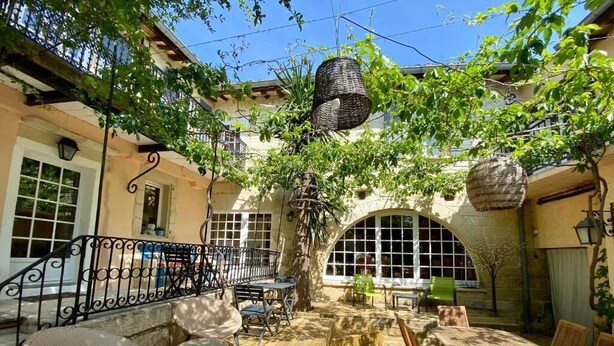 An outdoor patio with wicker furniture, a wooden table, and a hanging basket. - La Paillère (Mus)