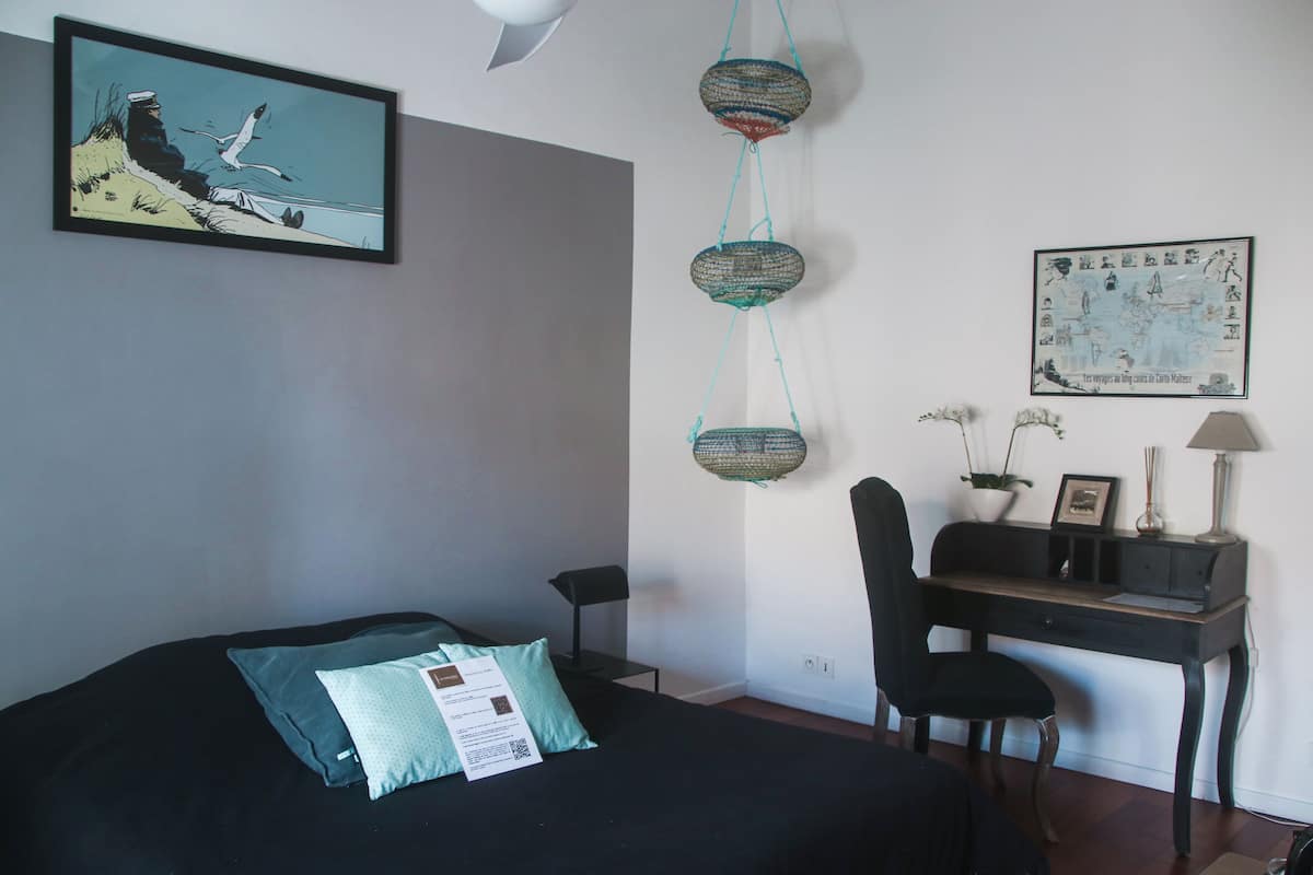 A bedroom with a bed, a desk, and a chair. There are wall decorations including a framed picture and a map.