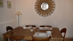 A dining area with a wooden table set for four, surrounded by wooden chairs. A large sunburst mirror hangs on the wall above the table. - La Paillère (Mus)