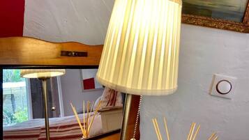 Eine Lampe mit einer plissierten Schirm, ein Nachttisch aus Holz und ein Spiegel, der einen Teil des Raumes reflektiert.