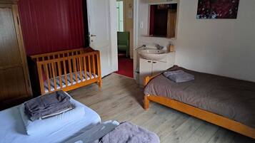 A bedroom with two beds, a wooden crib, a bathroom with a sink and mirror, and a red wall.