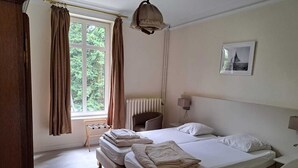 A hotel room with a large bed, a chair, a radiator, and a window with curtains. - Villa Elie (Malmedy)