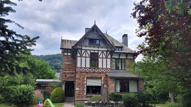 A Tudor-style house with a stone facade, a steeply pitched roof, and a small front yard with a pathway leading to the entrance. - Villa Elie (Malmedy)