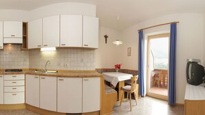 A kitchen with white cabinets, a sink, and a dining area with a table and chairs. - Paderlafoderhof Apartment 1, Zentrale Lage mit Garage (Lajen)