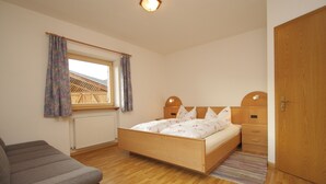 A bedroom with a wooden bed, a wooden nightstand, a chair, a window with curtains, and a radiator. - Paderlafoderhof Apartment 1, Zentrale Lage mit Garage (Lajen)