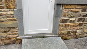 A white door with a small step leading up to it, set against a stone wall with a mix of brown and gray stones.