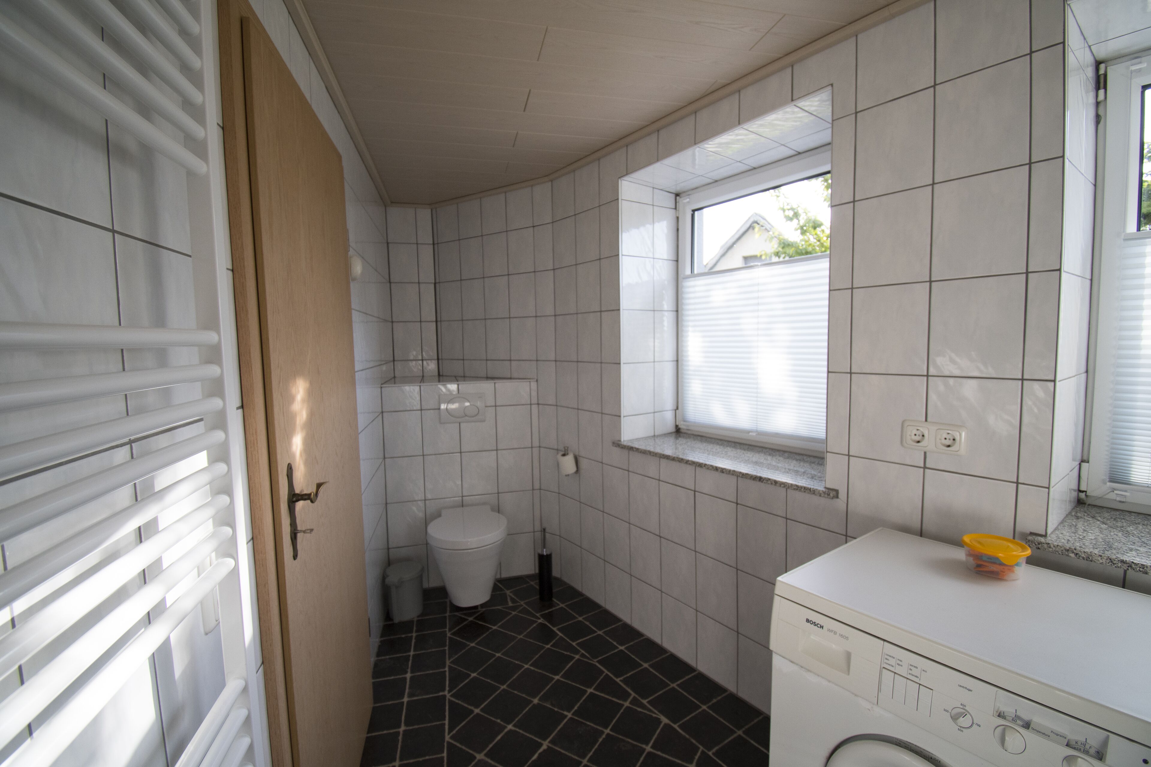 Pieni kylpyhuone, jossa on wc, pesukone ja ikkuna.