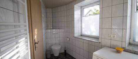 Pieni kylpyhuone, jossa on wc, pesukone ja ikkuna.