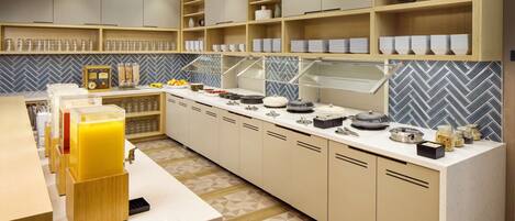A modern kitchen with built-in shelves, a fruit bar, and a herringbone tile backsplash.