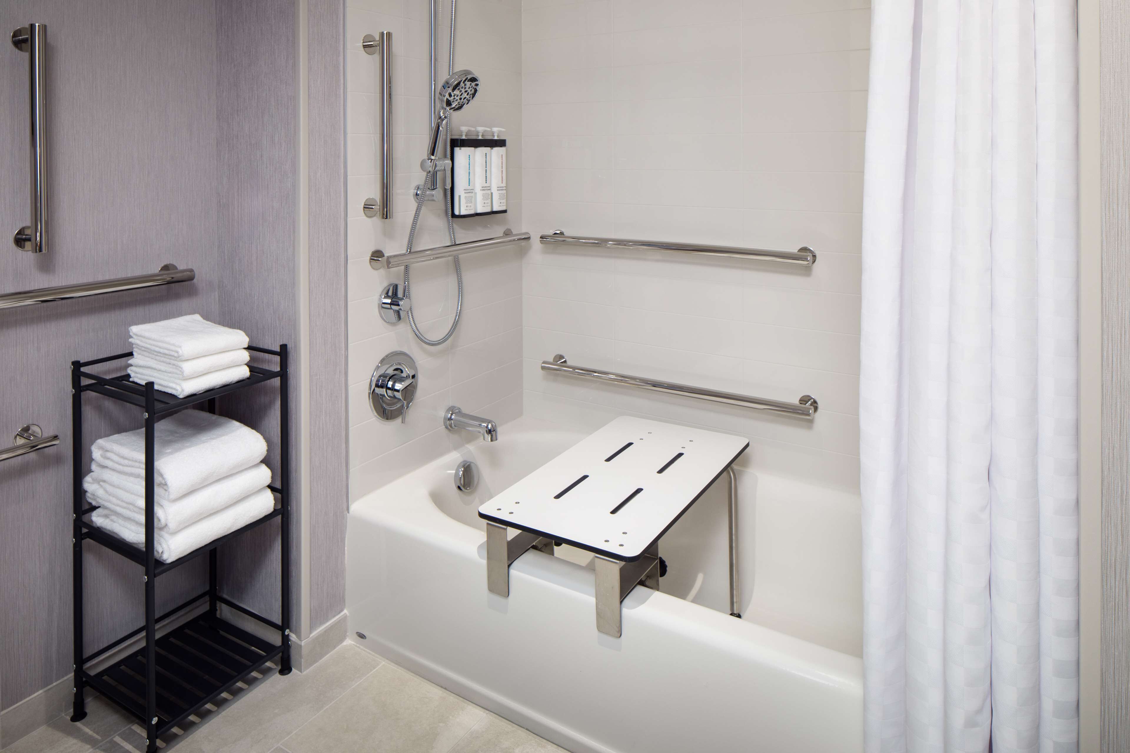 Une salle de bain moderne équipée d’une baignoire, de barres d’appui, d’un porte-serviettes et d’un pommeau de douche.