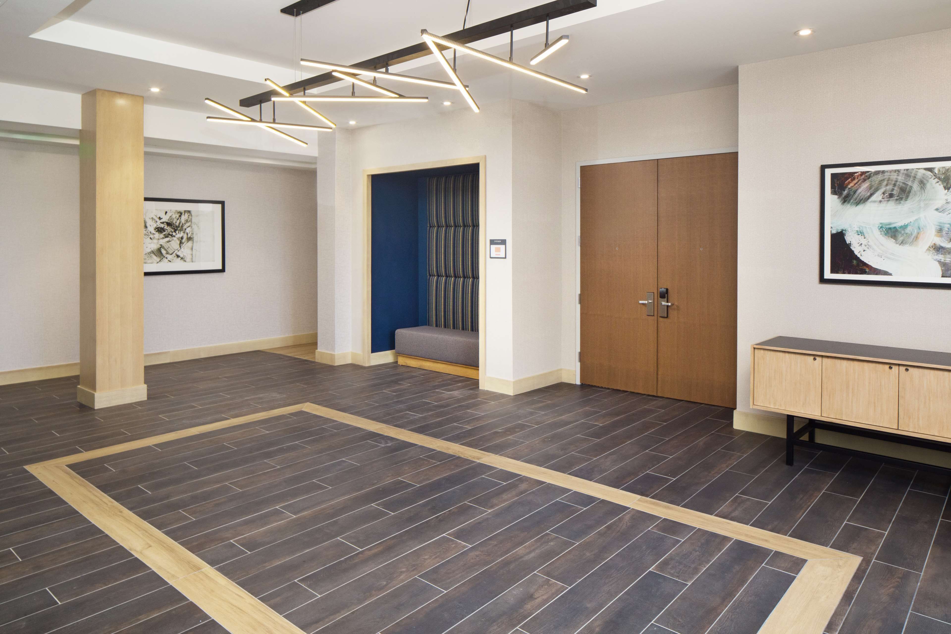 Un vestíbulo espacioso con piso de madera oscura, un banco de madera, una puerta grande de madera y una obra de arte enmarcada en la pared.
