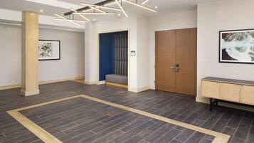 A spacious lobby with a dark wood floor, a wooden bench, a large wooden door, and a framed artwork on the wall.