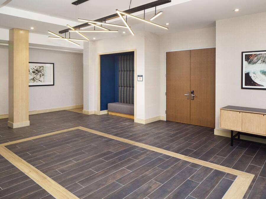 A spacious lobby with a dark wood floor, a wooden bench, a large wooden door, and a framed artwork on the wall.