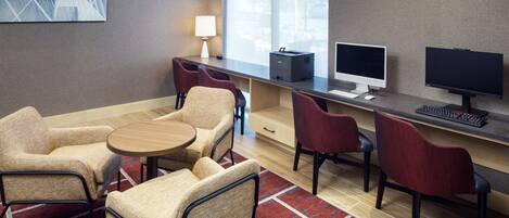 Una habitación de hotel moderna con un escritorio, dos sillas, una mesita, una lámpara y un equipo informático.