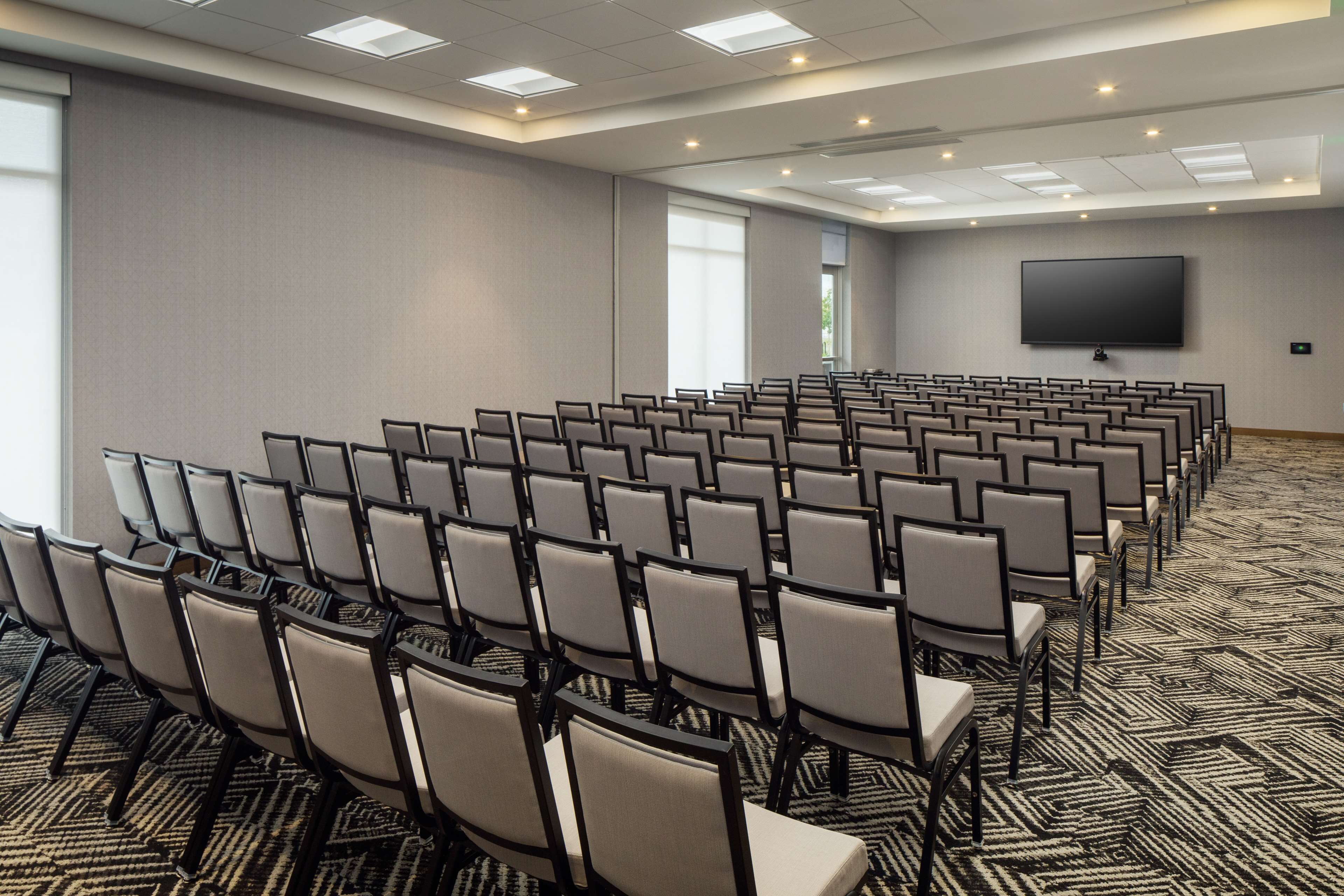 A conference room with rows of chairs, a large screen, and carpeted flooring.