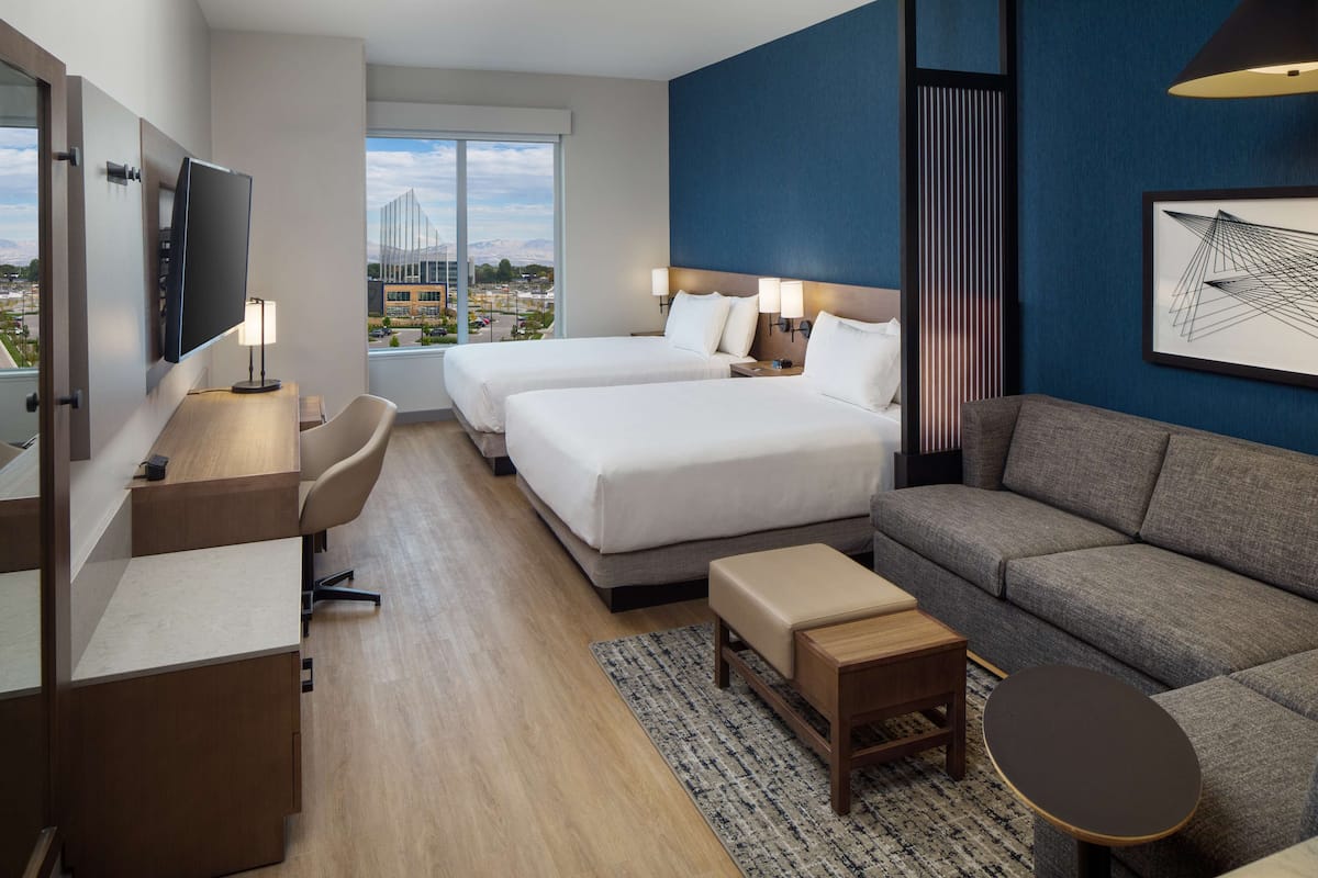 A hotel room with two beds, a sofa, a desk, and a TV.