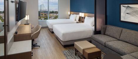 A hotel room with two beds, a sofa, a desk, and a TV.