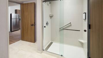 Un baño moderno con ducha de vidrio, una puerta de madera y un refrigerador de acero inoxidable en la habitación contigua.