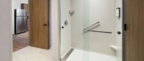 A modern bathroom with a glass-enclosed shower, a wooden door, and a stainless steel refrigerator in the adjacent room.