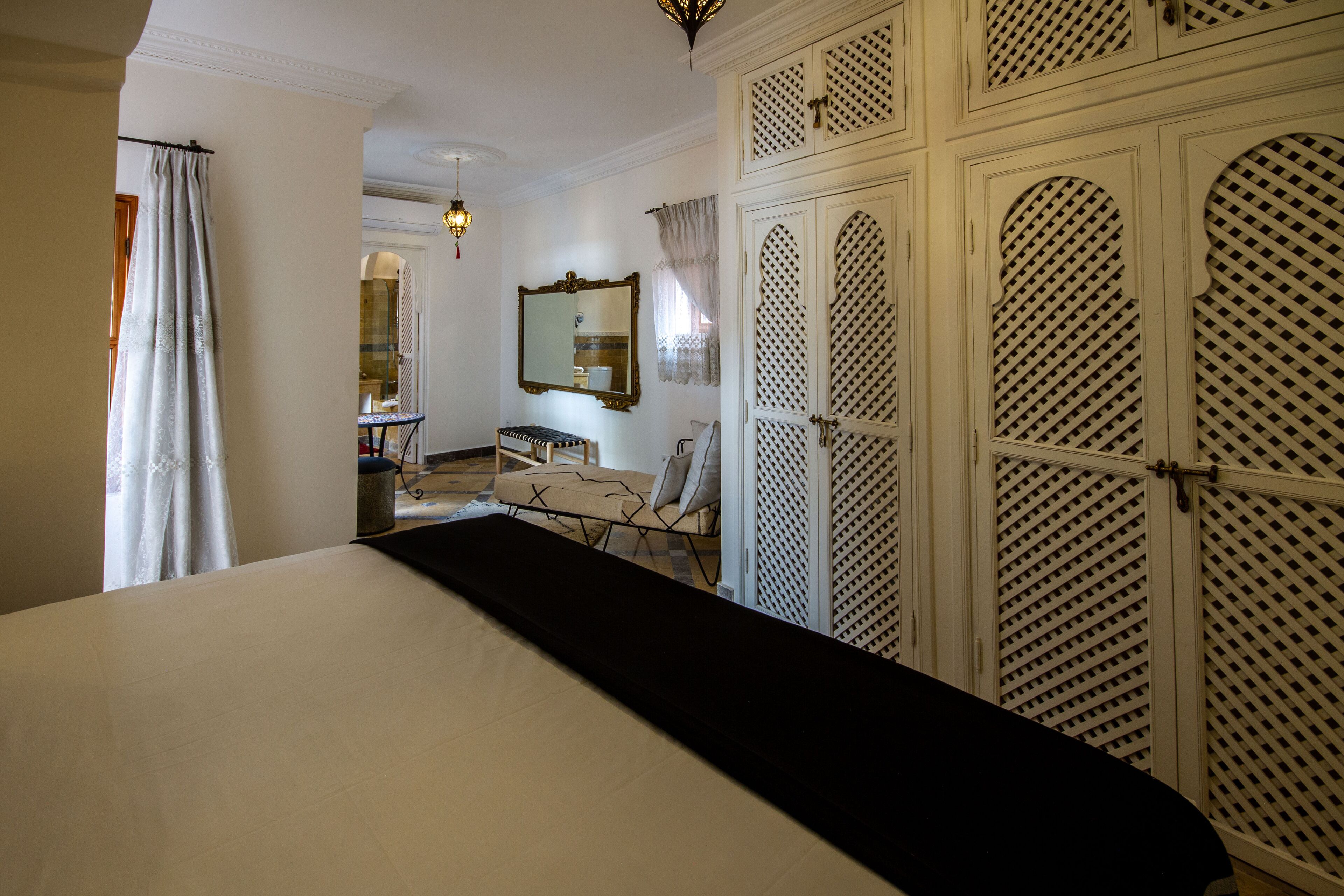 A bedroom with a large bed, a desk, a chair, a wardrobe, and a mirror.