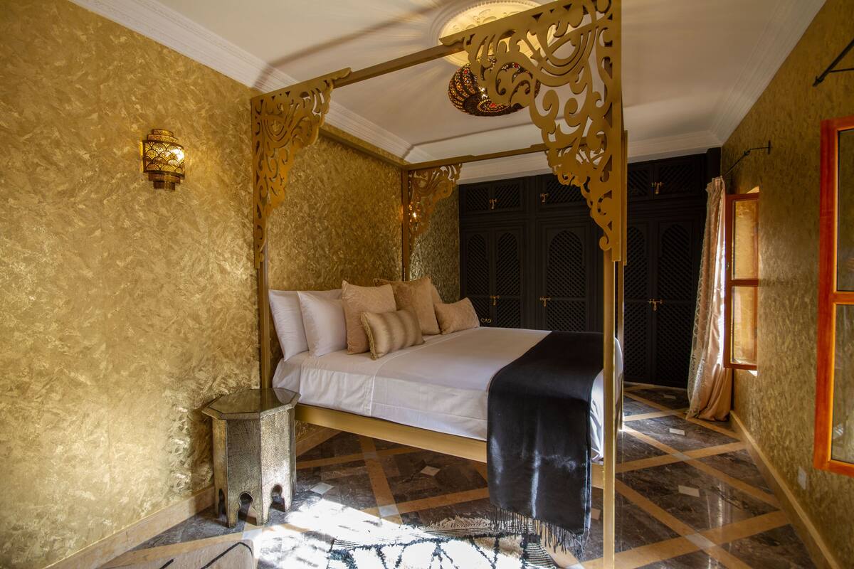 A luxurious bedroom with a large bed, ornate gold decor, and a patterned floor.