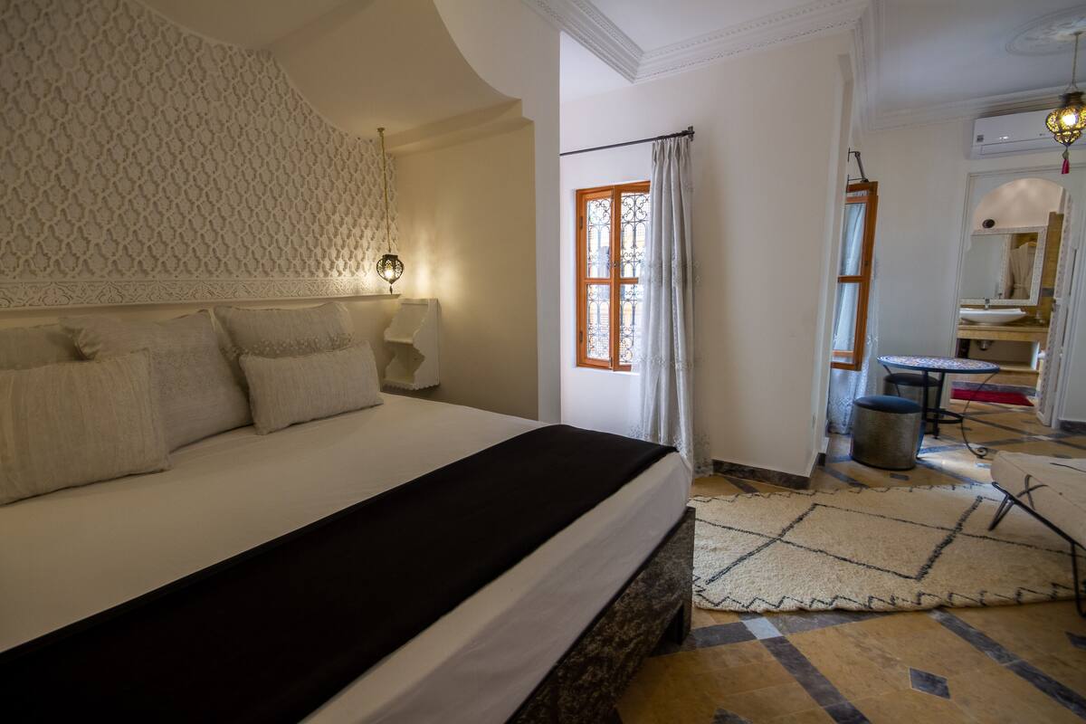 A hotel room with a large bed, a desk, a chair, and a window with curtains.