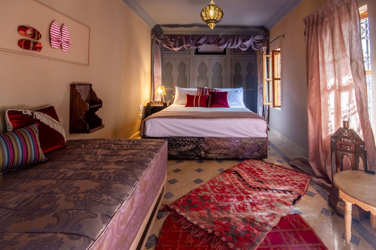 A traditional room with a bed, a sofa, a wooden table, and a patterned rug.