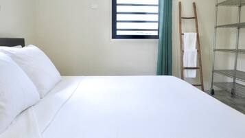 A neatly made bed with white linens, a window with horizontal blinds, a wooden ladder leaning against the wall, and metal shelves.