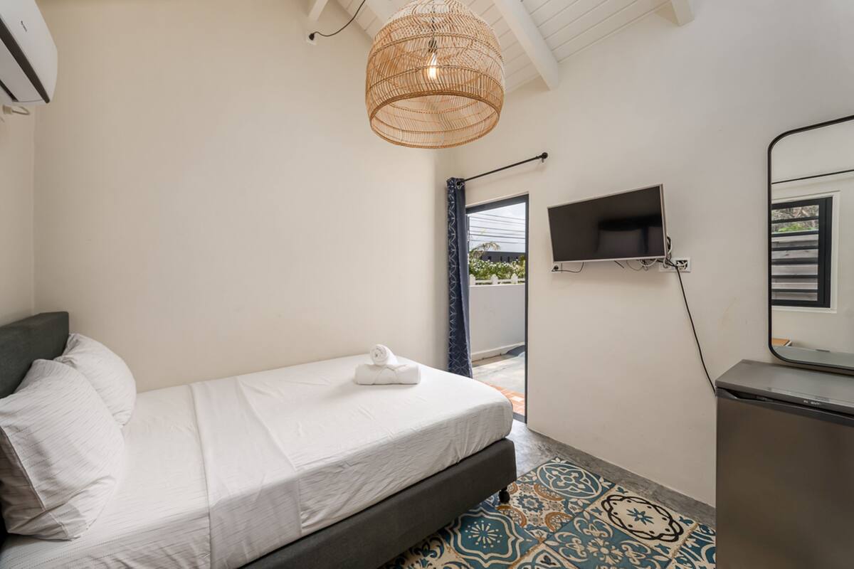 A bedroom with a bed, a television mounted on the wall, and a small desk.
