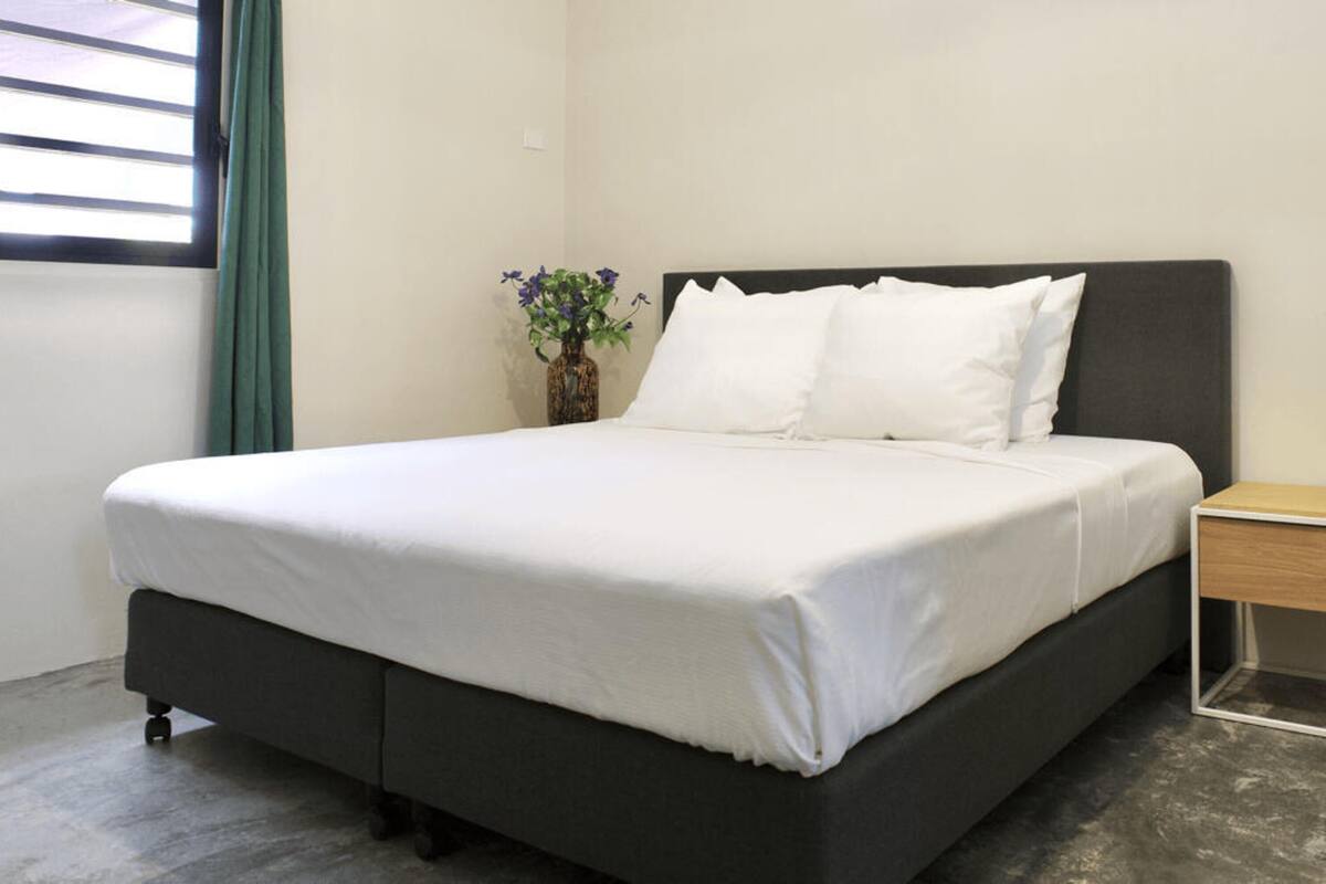 A neatly made bed with white linens, a dark headboard, and a small bedside table with a vase of flowers.