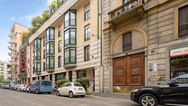 A street with parked cars and a building with a large wooden door and a sign that reads "COMPRE VEND". - Modern Loft in Porta Venezia (Milan)