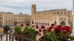 A balcony with potted geraniums, overlooking a historic building with classical architecture and a clock tower. - Sant Oronzo Apartment (Lecce)