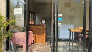 A reception area with a wooden desk, a table with a red checkered tablecloth, and a glass door leading to a dining area with tables and chairs. - Instyle place (Chiang Rai)