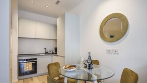 A modern kitchen with white cabinets, a built-in oven, and a dining area with a glass table and two chairs. - Milan Luxury Gem (Milan)