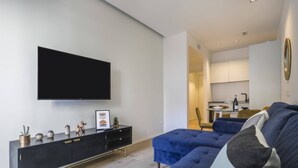 A modern living room with a large flat-screen TV, a dark-colored sofa, and a minimalist black console with decorative items. - Milan Luxury Gem (Milan)