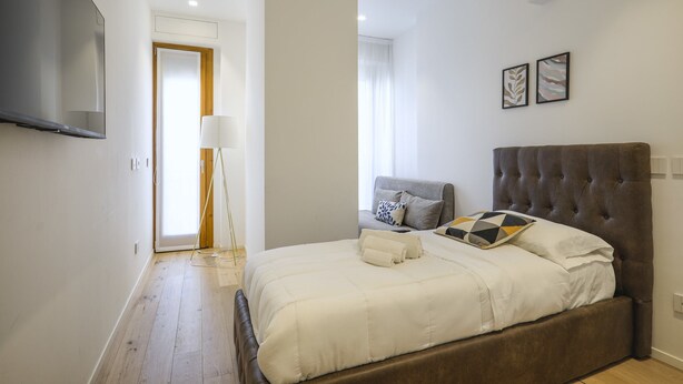 A bedroom with a large bed, a flat-screen TV mounted on the wall, a bedside table, and a lamp. - Milan Luxury Gem (Milan)