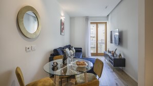 A modern living room with a glass dining table, a sofa, a TV, and a large mirror on the wall. - Milan Luxury Gem (Milan)