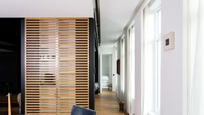 A modern interior with a dining area featuring a round table and chairs, a wooden slatted partition, and a hallway with a bed and a chair. - Magnificent High-end 2-bedroom Apartment in Gent (Ghent)